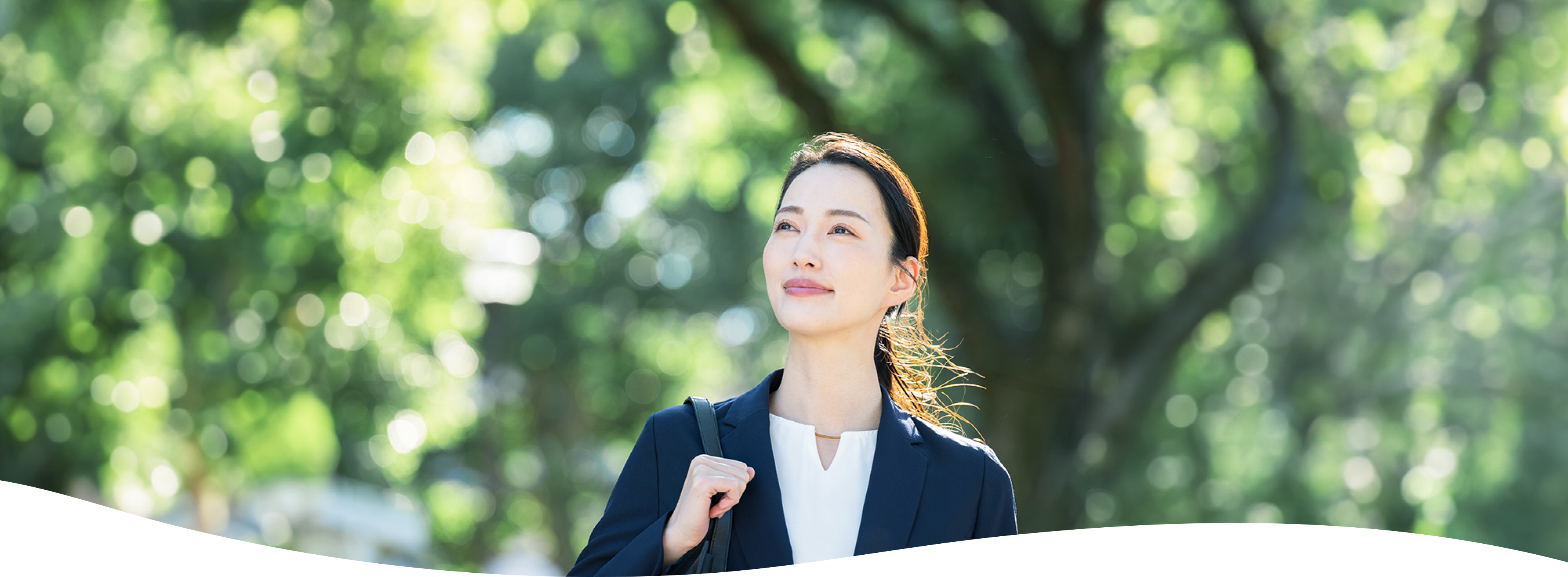 木々を背景にしたスーツの女性